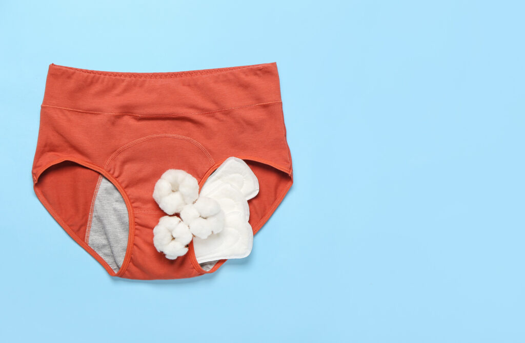 period panties, pads and cotton flowers on color background